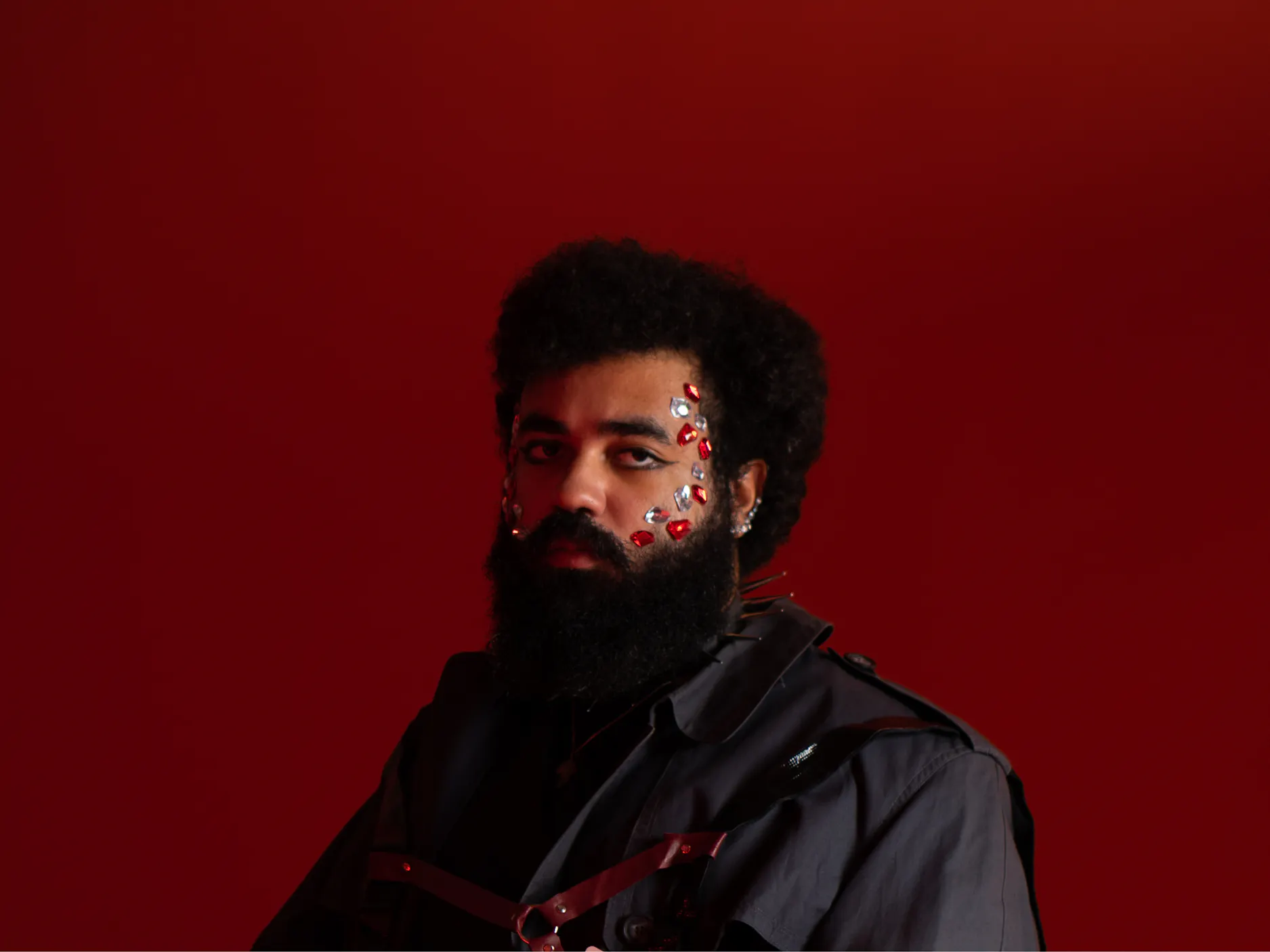 Studijska fotografija Tschimyja na rdečem ozadju, na obrazu ima večje bleščice